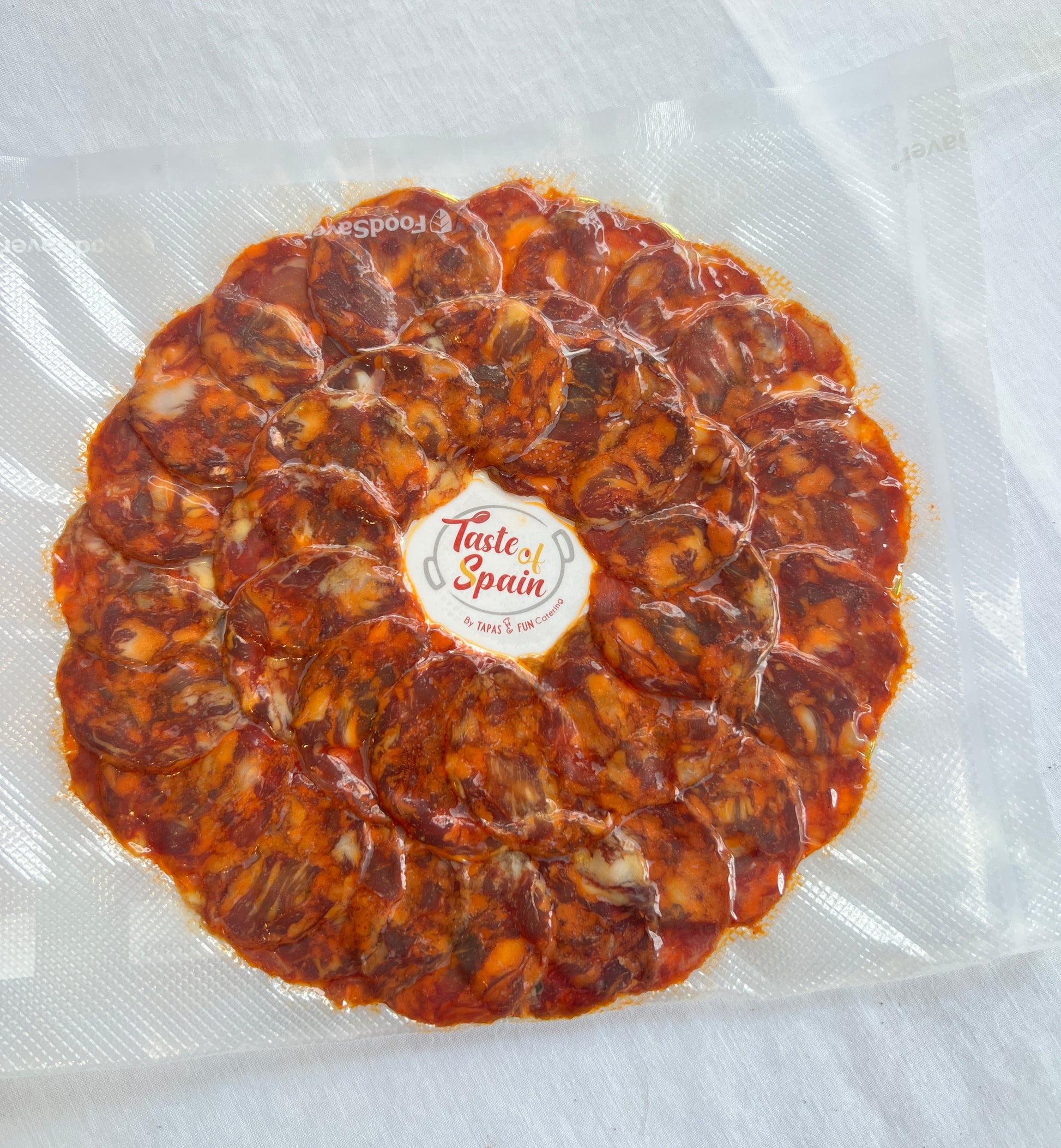 Round display of cured meat with 'Taste of Spain' label on a clear background