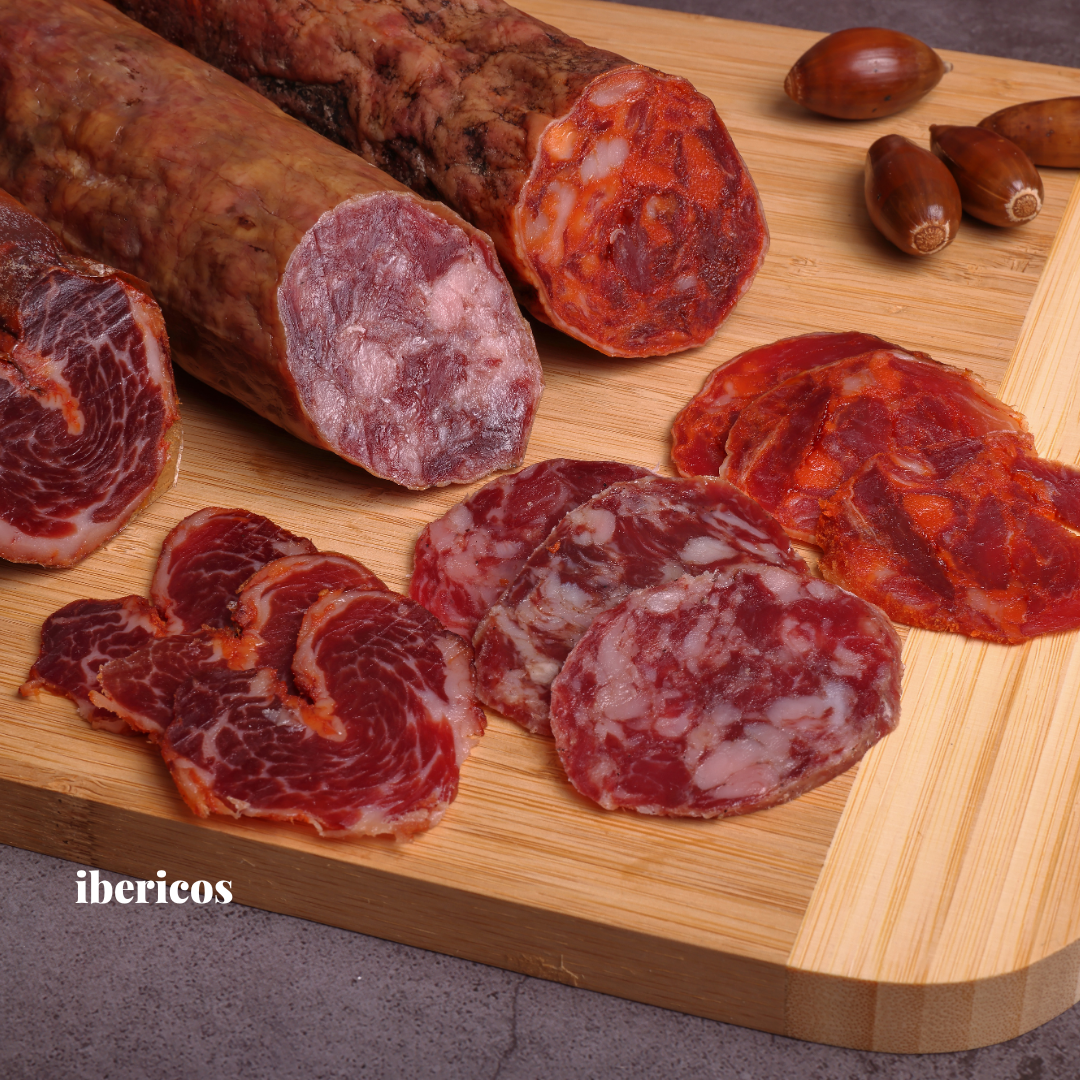 Assorted cured meats on a wooden cutting board with 'ibericos' branding.