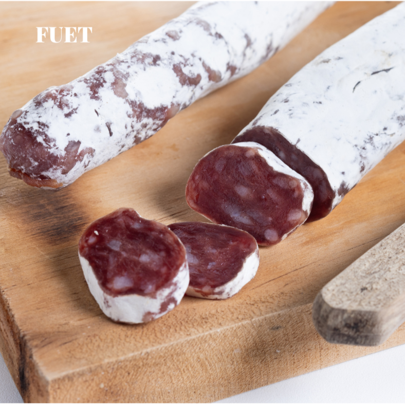 Sliced Fuet salami on a wooden board with a knife.